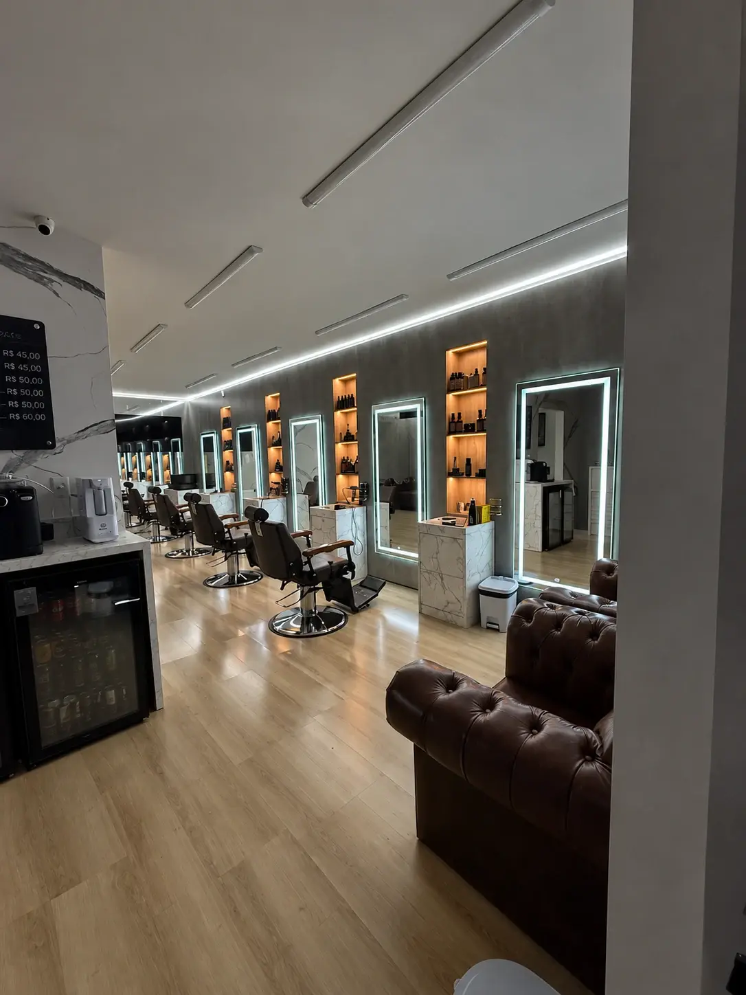 Salão da Barbearia Los Feras com cadeiras enfileiradas e espelhos iluminados